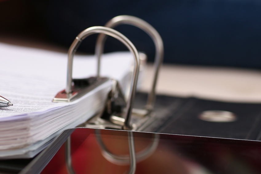 A close-up of a binder sitting on the desk. The binder is open to the first page with a blue pen sitting on top.